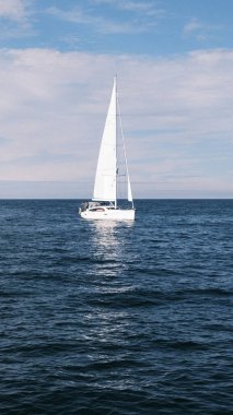 A single yacht sails with grace on a vast canvas of ocean blue, epitomizing solitude and the essence of sailing. This photograph captures the simple elegance of a solo nautical journey against the infinite horizon.