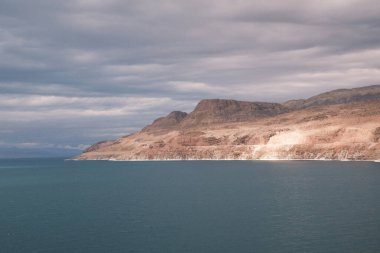 This captivating image showcases the tranquil beauty of the Dead Sea, bordered by the rugged mountains of Jordan. The serene waters reflect the soft glow of sunlight, offering a sense of calm and solitude. A perfect visual for conveying themes of nat