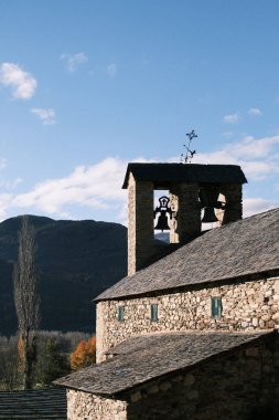 The historic bell tower of a stone church casts a majestic silhouette against the mountains and sky, a cultural icon rooted in the rich heritage of Spain's mountainous landscape.