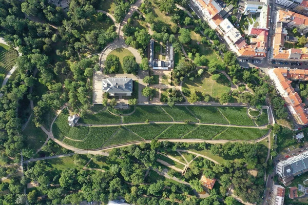 An aerial drone view reveals a serene Havlickovy Sady green park with a central amphitheater in the heart of Prague, highlighting the city's commitment to green spaces and cultural venues. The layout of the park offers a natural retreat and a space f
