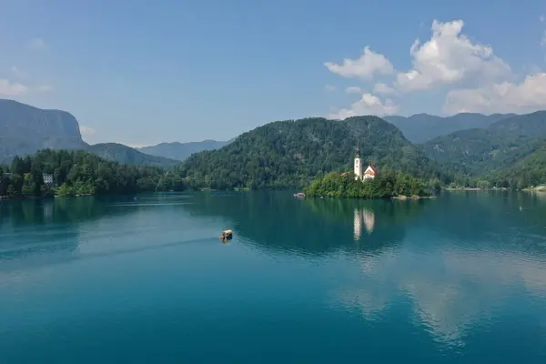 This drone image showcases the serene beauty of the Bled Island Church against the backdrop of the calm reflective waters of Lake Bled, offering a peaceful escape.