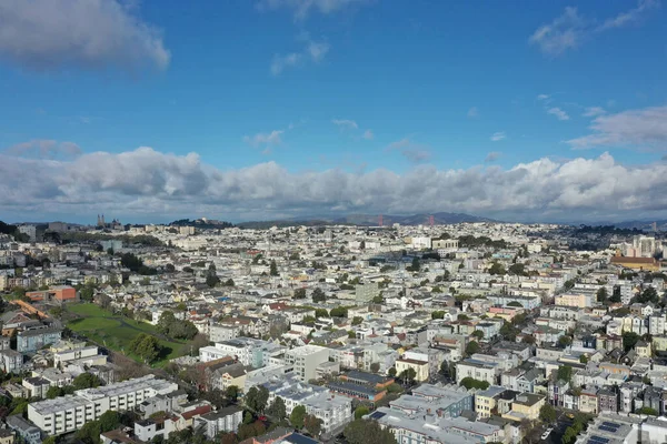 This drone image showcases the iconic San Francisco skyline under a dramatic cloudy sky, with the city's streets leading towards the bustling downtown area.
