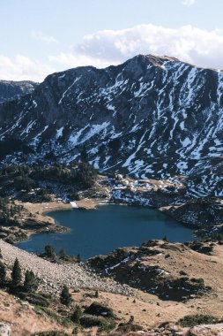 The grandeur of the snow-clad peaks overlooking a serene Pyrenean lake captures the untouched essence of Spain's natural landscapes, inviting onlookers to bask in its rugged beauty.