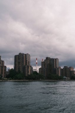 Gloomy clouds hang over the high-rise riverside apartments in New York City, depicting the city's dense living spaces against the forces of nature.