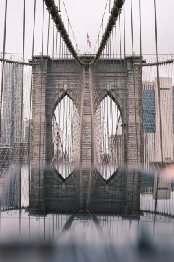 The iconic stone arches of the Brooklyn Bridge echo in the serene waters below, a peaceful yet powerful reflection of one of New York City's historic landmarks.