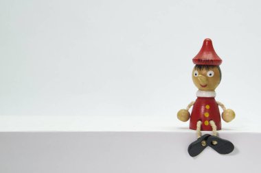 Pinokyo, tahta oyuncak uzun burunlu bir çocuğu temsil ediyor, sade, izole beyaz bir arka planda oturuyor..