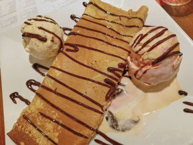 Lucuma, vanilya ve çikolatalı şekerle süslenmiş çilekli dondurma eşliğinde içi pelte dolu krep.