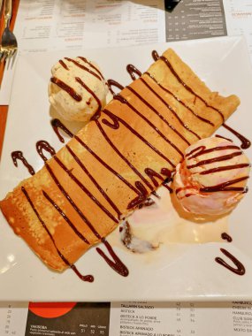 Lucuma, vanilya ve çikolatalı şekerle süslenmiş çilekli dondurma eşliğinde içi pelte dolu krep.