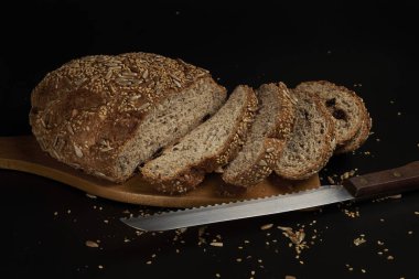 Koyu bir zemin üzerinde çoklu tahıl tohumlarıyla evde yapılan ve pişirilen zanaatkar ekmek, aileyle birlikte yemek için sağlıklı bir ürün..