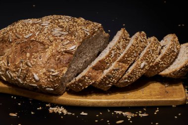 Koyu bir zemin üzerinde çoklu tahıl tohumlarıyla evde yapılan ve pişirilen zanaatkar ekmek, aileyle birlikte yemek için sağlıklı bir ürün..