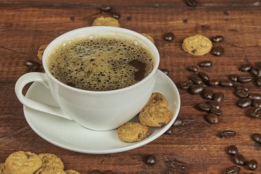 Bir fincan lezzetli gurme kahve ve yanında gevrek kurabiyeler ve eski ahşap bir arka planda kavrulmuş kahve çekirdekleri.