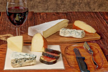 Bir bardak kırmızı şarap eşliğinde, farklı peynirlere sahip, harika aromalı ve dokulu bir tahta..