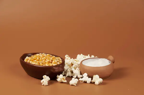 Kırsal seramik bir kabın içindeki altın mısır taneleri, kıtır kıtır patlamış mısırı hazırlamak için ana malzeme, yanında da bir kavanoz tuz.