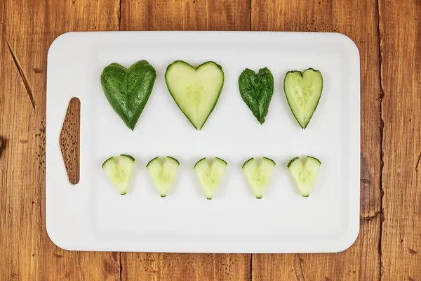 Salatalık eski ahşap arka planı olan beyaz bir tahtanın üzerinde kalp şeklinde kesilmiş.