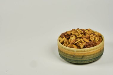 Beyaz bir arka planda, kamış sepetli taşlama kabında çeşitli fındıklar. Badem, Ceviz, Ceviz ve Kestane