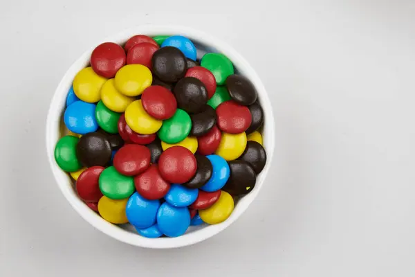 Farklı renklerde karamelaya bulanmış çikolata fıçıları, beyaz arka planda bir kabın içinde.