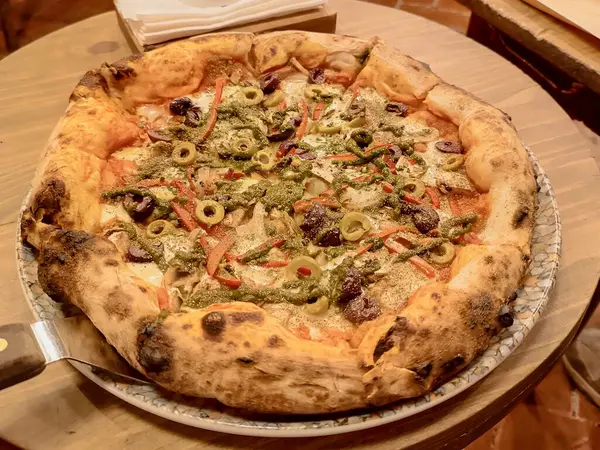 Etli, çeşitli sebzeli ve ahşap bir masada renkli bir tabakta servis edilen mozarella peynirli bir pizza.