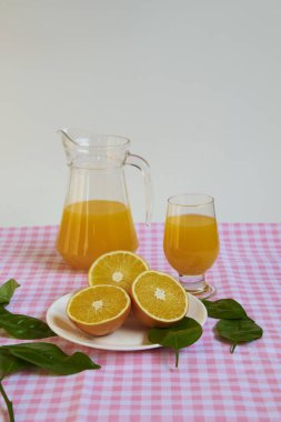 Taze sıkılmış portakal suyu, ferahlatıcı ve sağlıklı, yeşil yapraklarla süslenmiş, pembe ve beyaz kareli masa örtüsü olan bir masada..