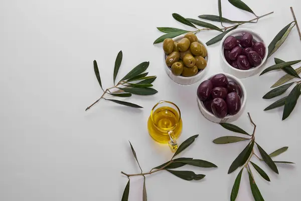Yuvarlak kaselerde siyah ve yeşil zeytinler, beyaz bir zemin üzerinde zeytin yaprakları ile metin için boşluk ile