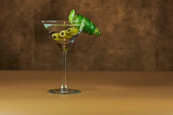 İçi yeşil zeytinli Martini bardağını sıcak renkli bir yüzeye serinletiyor..