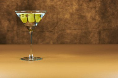 İçi yeşil zeytinli Martini bardağını sıcak renkli bir yüzeye serinletiyor..