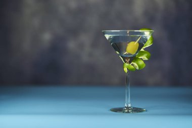 İçi yeşil zeytinli martini bardağı, mavi ve gri bir gökyüzünde
