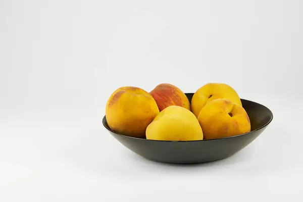 Şeftaliler yakın plan siyah bir plaka üzerinde izole edilmiş, fotokopi alanı ile hafif bir arkaplan üzerinde düzenlenmiş.