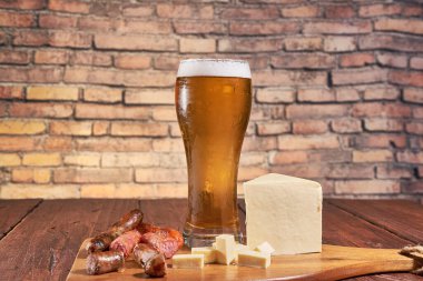 Bir bardak buzlu altın bira, yanında da peynir ve bira sosisi aperatifi..