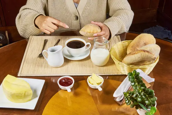 Ekmek, kahve, süt, reçel, tereyağı ve peynirle mutfakta sağlıklı bir kahvaltı yapan bir kadının yakın çekimi..