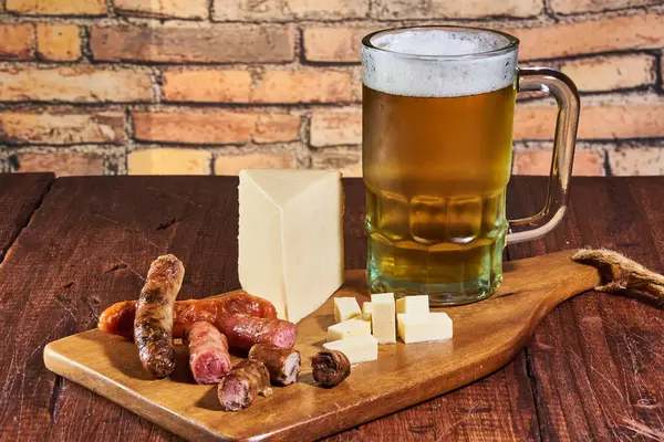 Bir bardak buzlu altın bira, yanında da peynir ve bira sosisi aperatifi..