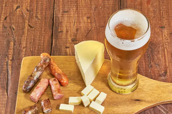 Bir bardak buzlu altın bira, yanında da peynir ve bira sosisi aperatifi..