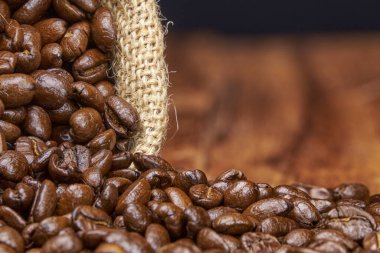 Kavrulmuş kahve çekirdekleri bir jüt torbasından kırsal ahşap bir yüzeye dökülüyor..