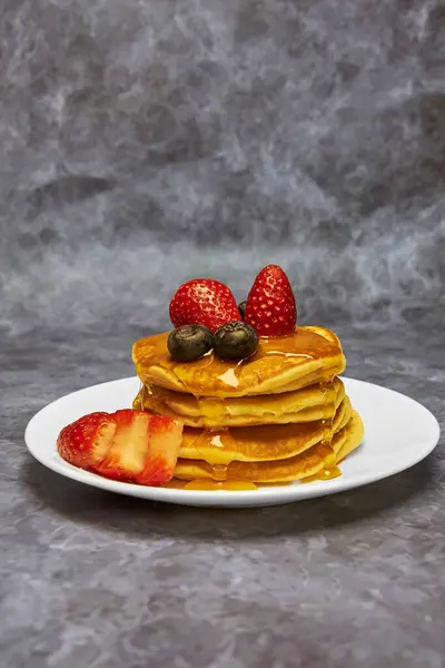 Şahane bir kahvaltı için lezzetli akçaağaç şurubuyla süslenmiş yaban mersini ve taze çilekle süslenmiş, pudra şekerli bir kulede bir tabak lezzetli krep..