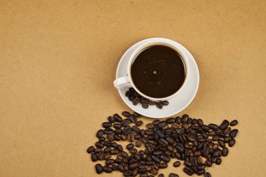 Kahve fincanı, yakın plan, taze kavrulmuş fasulyeyle birlikte, kopyalanmış ahşap bir masa üzerine dökülmüş.