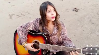 Güzel bayan müzisyen kumsalda akustik gitar çalıyor.