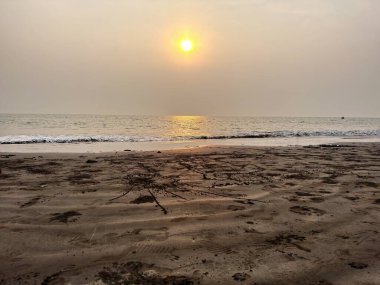 Sakin bir kumsalın üzerinde gün batımı yumuşak dalgalar ve kumdaki ayak izleri..