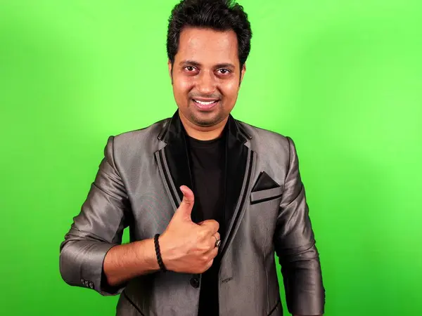 Confident man in a suit giving thumbs up and smiling against a green background.