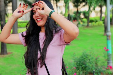 Neşeli bir kadın dışarıda gülüyor. Elleri yanağında. Arka planda yeşillik bulanıklaşıyor..