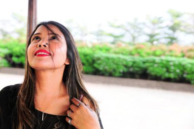 Arka planda bulanık yeşillik ile umut dolu bir yüz ifadesiyle gülümseyen kadın..