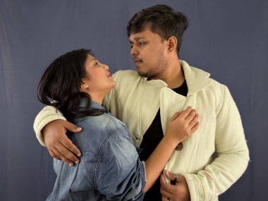 Birbirlerini kucaklayan ve gri bir arkaplanda birbirlerine bakan sevgi dolu bir çift..