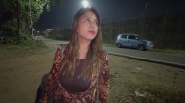 Issız bir sokakta sigara içen düşünceli genç bir kadın gecenin bir yarısı ayakta dikiliyor.