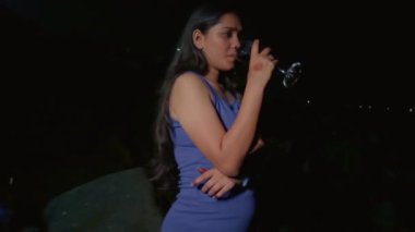 Loş bir çevrede şarap kadehinden alkol içen genç bir kadının portresi.