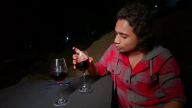 Gülümseyen adam bir bardak kırmızı şaraptan zevk alıyor. Geceleri bardaklarla konuşuyor. Neşeli bir ifadeyle dışarıda oturuyor.