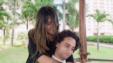 Mutlu çift, yemyeşil bir parkta bir kadının arkadan bir erkeği kucaklamasıyla mutlu bir şekilde şarkı söylüyor.