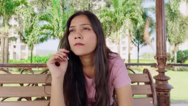 Nachdenkliche Junge Frau Sitzt Auf Einer Parkbank Inmitten Grüner Bäume — Stockvideo