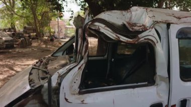 Şiddetli çatısı ve gövdesi hasar görmüş bir beyaz minibüs bir trafik kazası sonrası oluşan bir kazayı resmediyor.