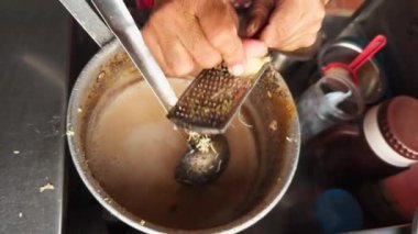 Yerel mutfağın özünü yakalayan kepçeyle büyük bir tencerede çay ya da kahve yapan bir sokak yemeği satıcısı. 