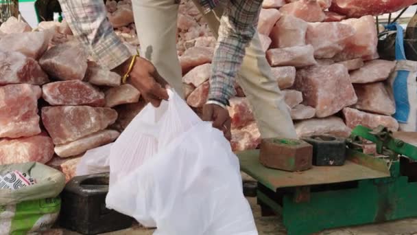 バックグラウンドのピンクのヒマラヤ塩の大きな山で市場でピンクの塩を販売する男 — ストック動画
