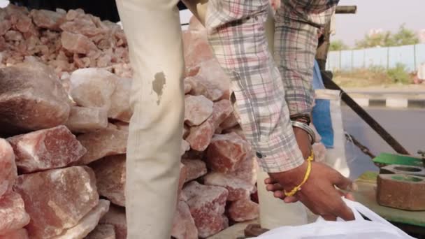 バックグラウンドのピンクのヒマラヤ塩の大きな山で市場でピンクの塩を販売する男 — ストック動画