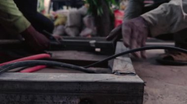 Metal boruları hizalamaya çalışan işçilerin ellerini kapatın. Fabrika atölyesinde demir pencere yapın.